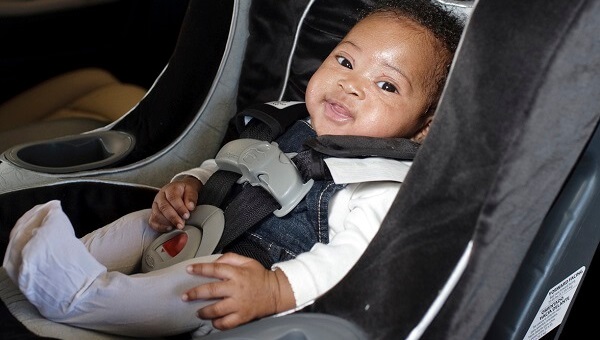 A smiling infant is sitting in his car seat.