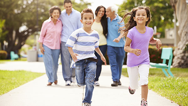 A young sister and brother are running while their parents and grandparents walk behind them.