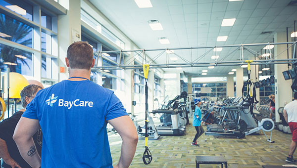 A trainer wearing a BayCare shirt talks to a member of the fitness center.