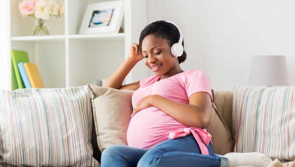 A pregnant woman is using headphones to listen to a podcast.