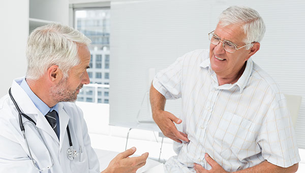 A male doctor is talking with a senior male patient who is pointing to his stomach area.