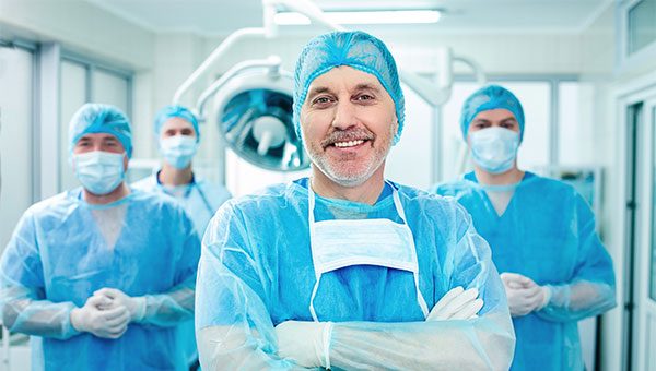 A smiling male surgeon stands near his colleagues
