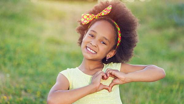 A little girl makes a heart shape using her hands