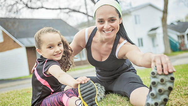 A mother and her young daughter sitting and stretching their legs outdoors.