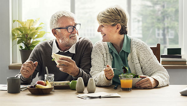 A senior couple smiling while eating breakfast together.
