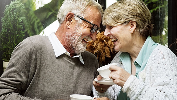 A senior couple laughing while drinking coffee together.