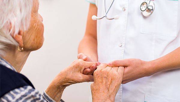 A female nurse holds the hands of a senior female patient while talking with her.