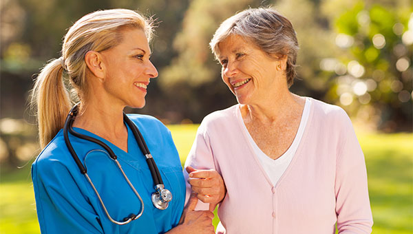 A smiling female nurse helps a senior female patient to walk outside.