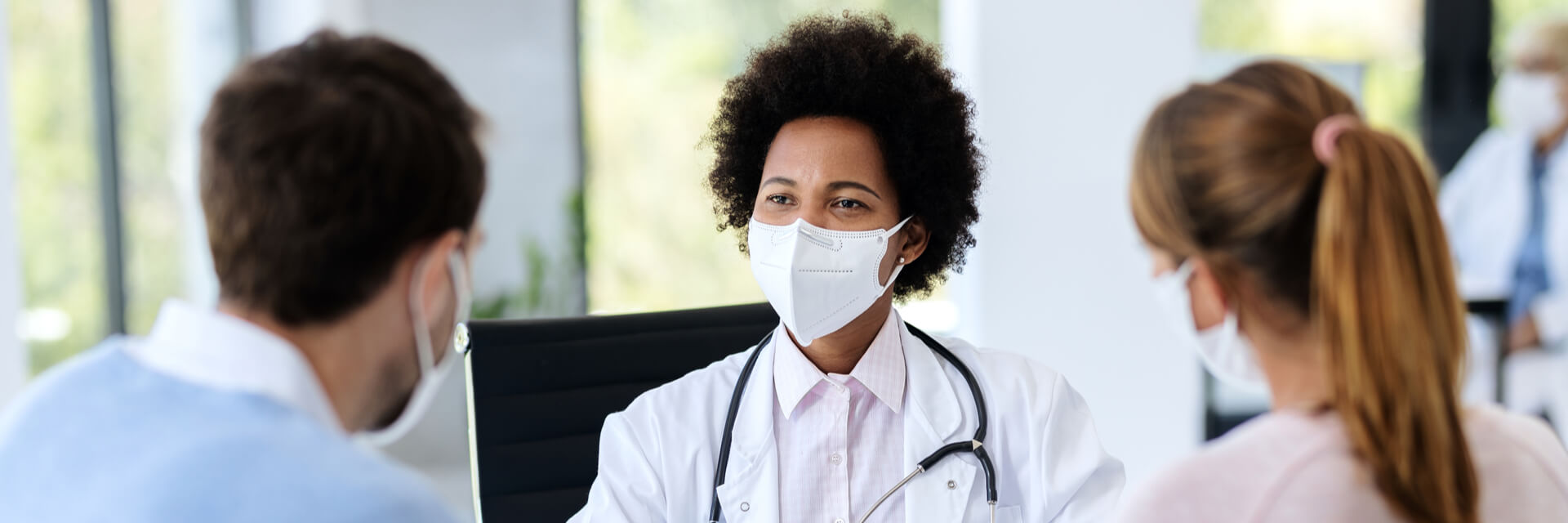 Black female doctor talking to a couple while wearing protective face mask