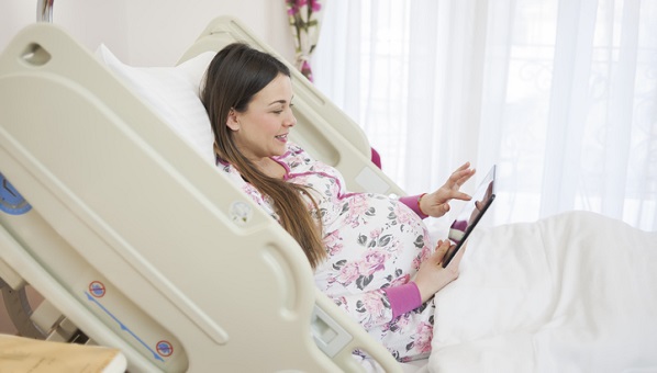 pregnant woman in hospital smiling with tablet