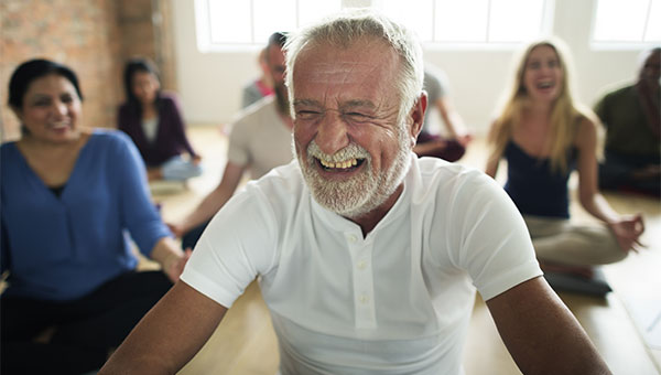 A senior man is laughing while taking a yoga class.