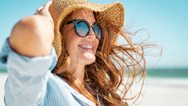 smiling woman holding her hat on at the beach