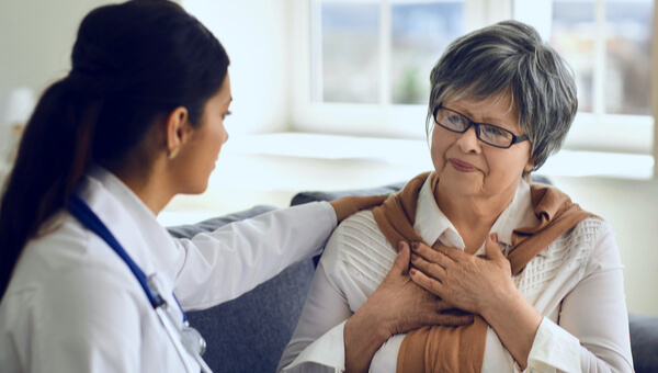 doctor sitting down with elderly woman with hands on chest