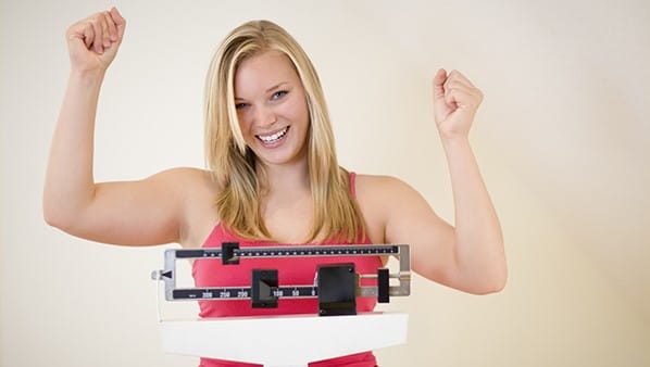 lady standing on a scale with her arms raised with success