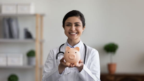 A young female health professional smiling while holding a piggy bank.