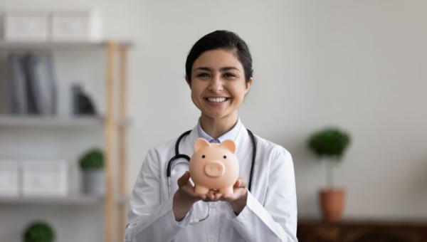 A young female health professional smiling while holding a piggy bank.
