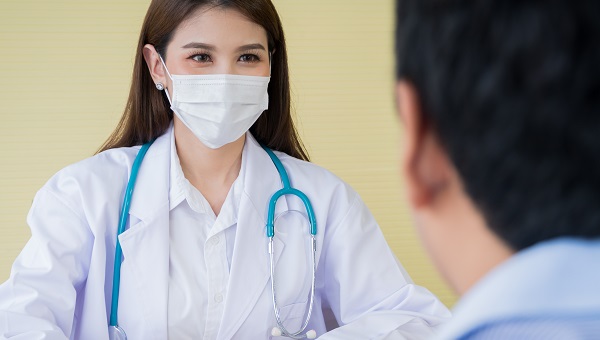 A female doctor is wearing a mask and talking to her male patient.