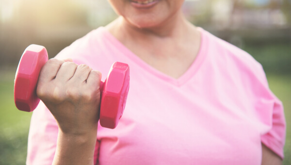 woman in pink shift lifting dumbbell