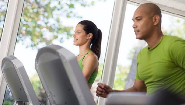 young adult man and woman wearing green and running on treadmills