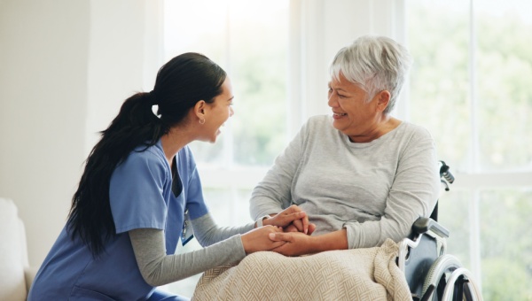 A nurse holds hands with a patient in a wheelchair.