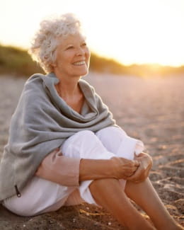 Senior woman sitting on the beach at sunset smiling
