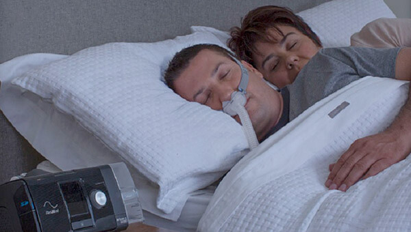 Couple in bed while man is using sleep apnea device on his face