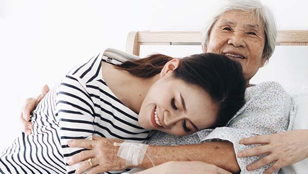 A woman is hugging her mother, who receives home infusion therapy.