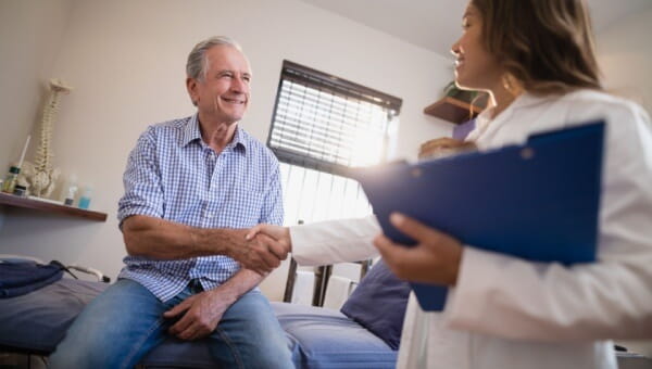 An elderly male patient shakes hands with his female doctor.
