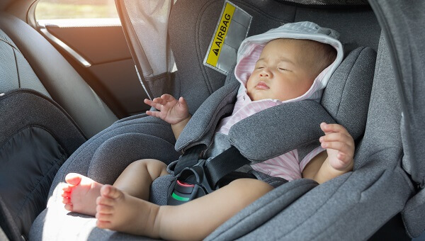 A baby is sleeping in her car seat.