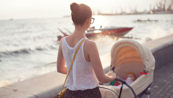 Young mom pushing a baby carriage by the water