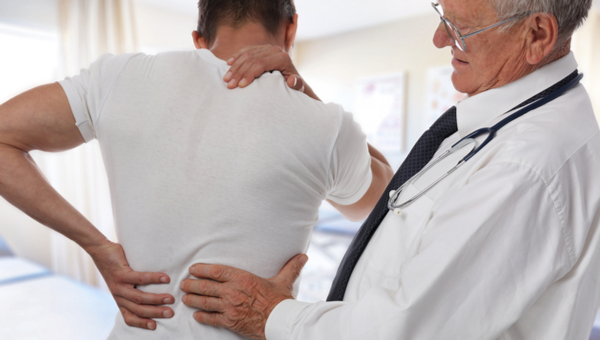 A male doctor examines a male patient's back.