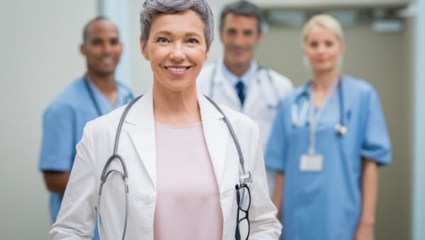 A woman in a hospital uniform stands before a group of doctors, focused on orthopedics.