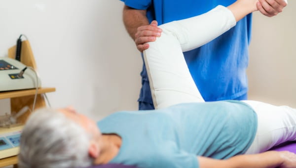 A patient lies on her back while a physical therapy assistant bends her knee.