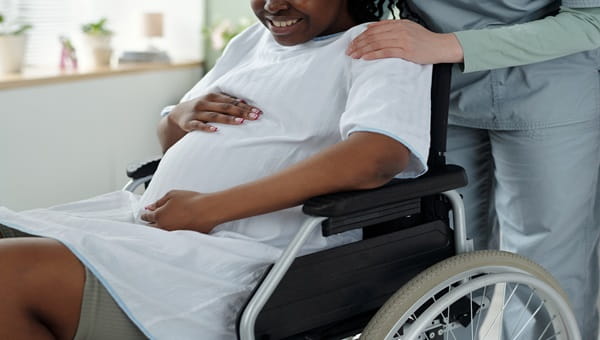 Pregnant woman being pushed around by nurse in a wheelchair while the woman is holding her stomach