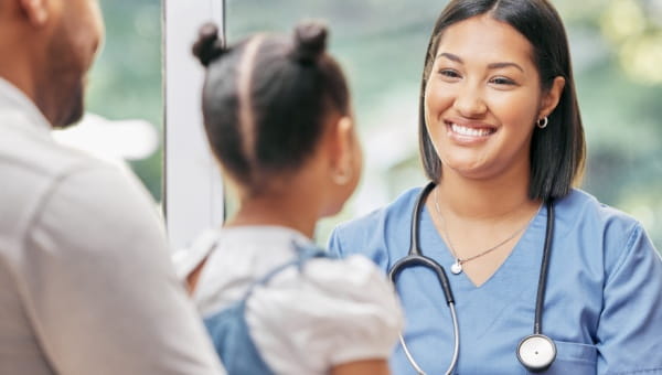 A nurse smiling at a young girl and her father