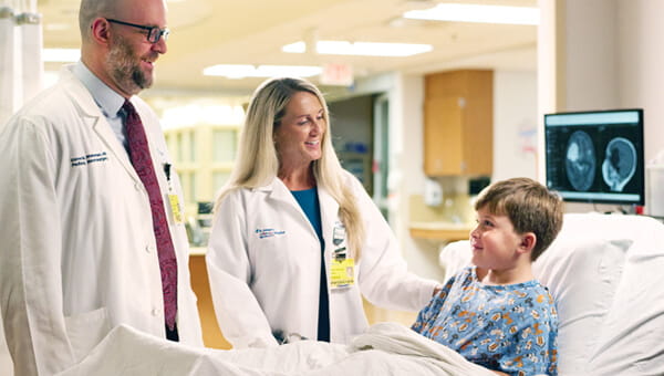 A little boy, who is a pediatric patient, is met at the bedside by two BayCare doctors and are talking to the patient