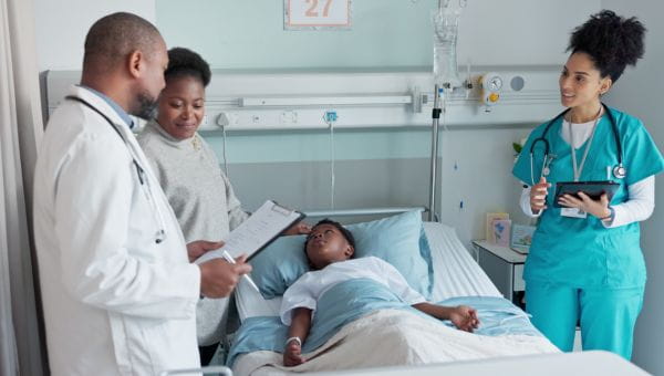 A child is in a hospital bed, and his mother is talking with a doctor and nurse.