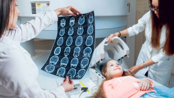 Two clinical team members are preparing a girl for a brain scan.