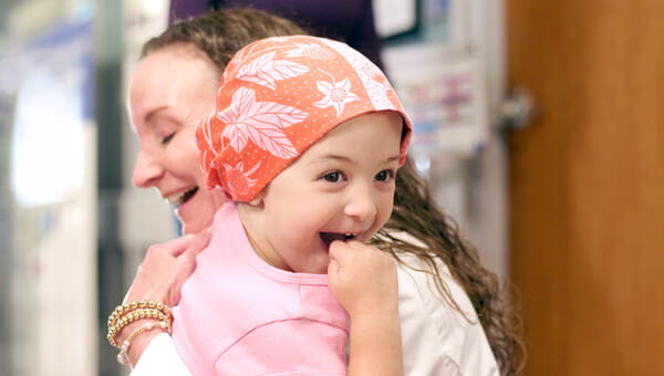 A female pediatric cancer patient hugs a doctor.
