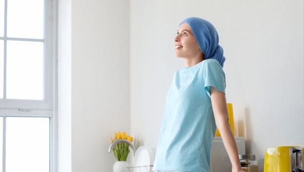 A teenage patient with a scarf covering her head standing in a kitchen and smiling. 