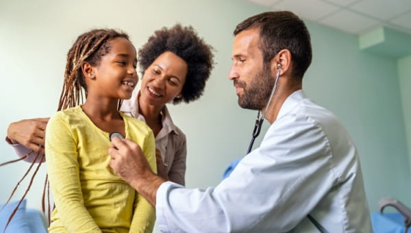 A pediatric doctor using a stethoscope on a pediatric patient with mom behind the patient
