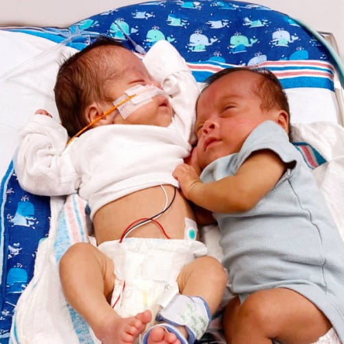 Two infants snuggling in a NICU bed.