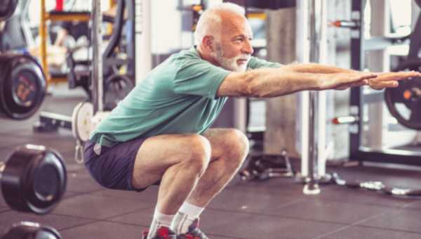 older man in gym performing a squat