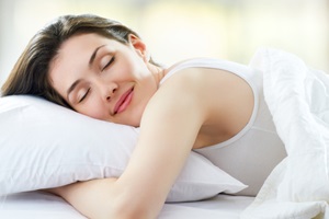 A young woman hugs a pillow and smiles as she sleeps