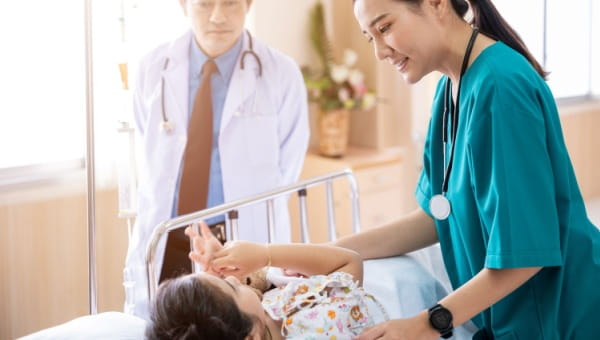 A doctor and nurse talking to a pediatric patient on a hospital bed before surgery.