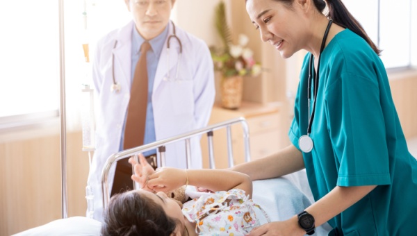 A doctor and nurse talking to a pediatric patient on a hospital bed before surgery.