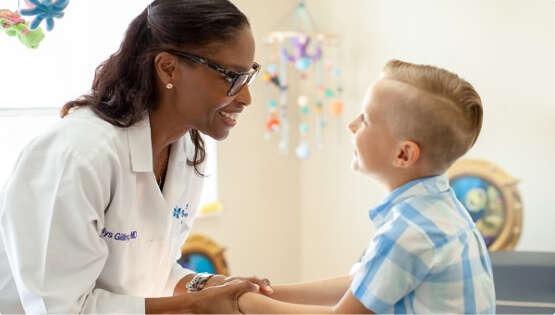A female BayCare pediatrician holding hands with a young boy in a bright hospital room setting.