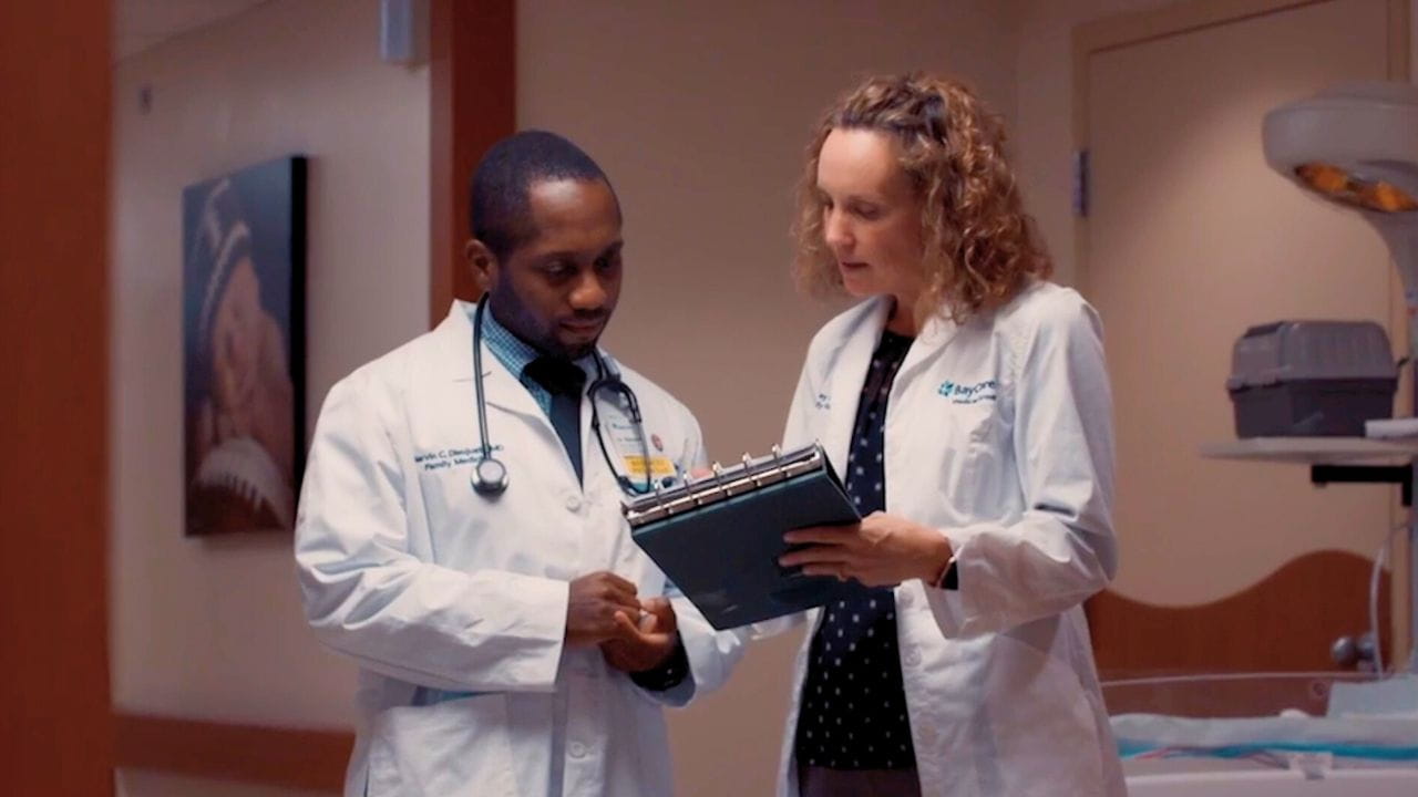 A faculty member shows a resident something on a clipboard.