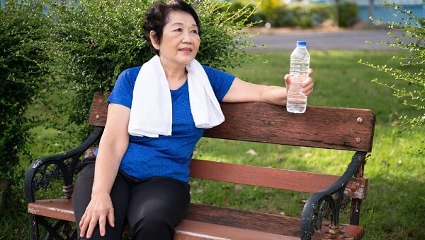 older woman sitting on park bench with water bottle in hand