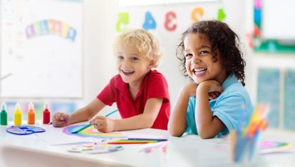 a smiling boy and girl painting a rainbow in a classroom